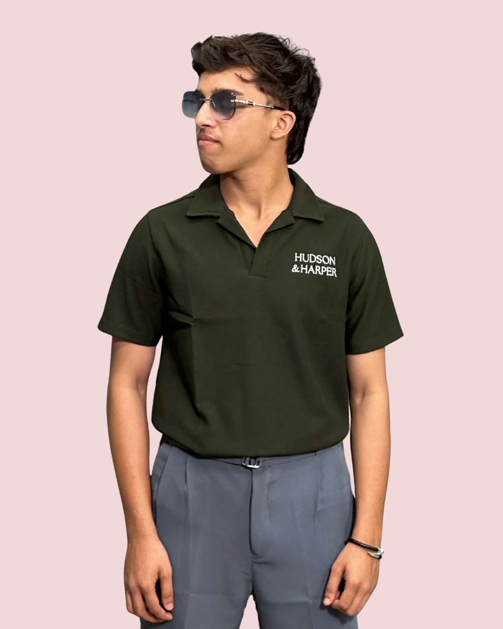 Person wearing a green polo shirt with 'Hudson & Harper' logo on a pink background