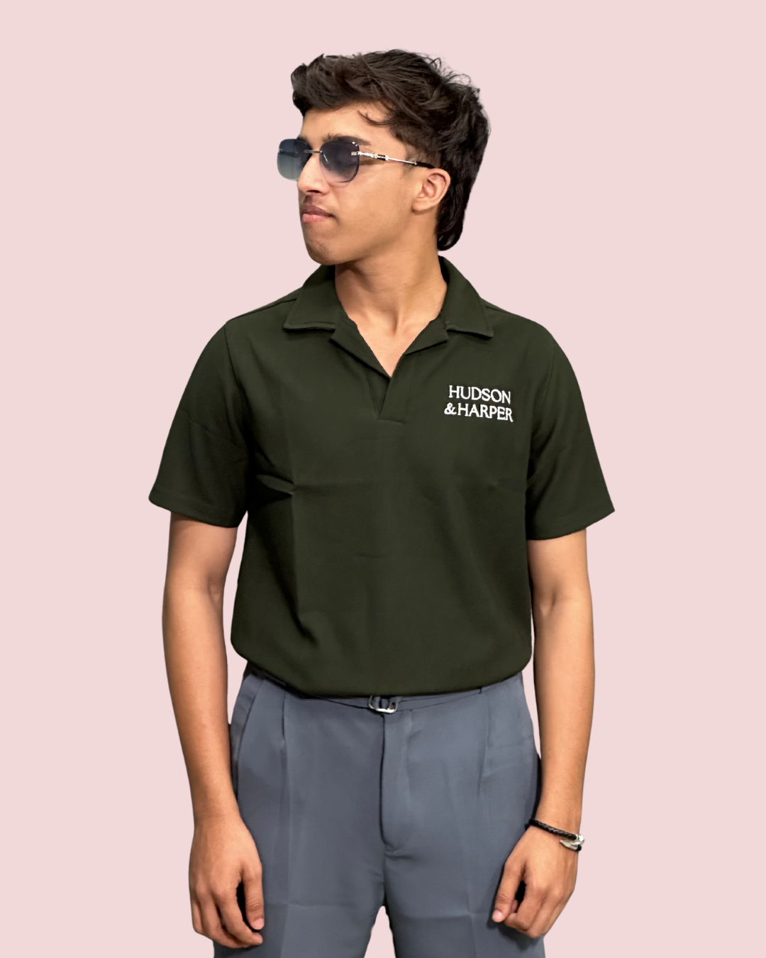 Person wearing a green polo shirt with 'Hudson & Harper' logo on a pink background